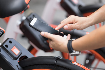 Hands using smartphone scanning the QR code of shared bike in city