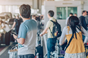 Passengers with big roller luggage stand to wait for the car to pick up at airport arrival terminal.