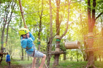 young boy passing cable route among trees, extreme sport in adventure park