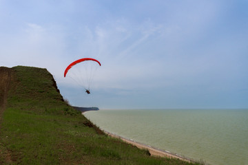 paragliding on a red paraglider flying over the sea