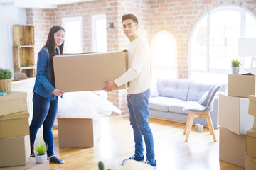 Beautiful young asian couple looking happy, holding a big cardboard box smiling excited moving to a new home