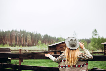 Girl in clothes with ethnic patterns posing against the background of the fence on an old farm,...