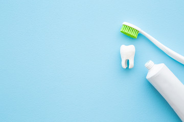 White tooth, tube of toothpaste and toothbrush with green bristle on pastel blue background. People...