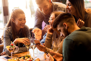 Group of young friends having fun in restaurant, talking and laughing while dining at table.