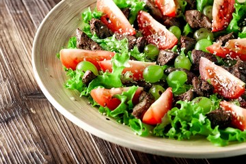 warm salad with chicken liver and grapes on a wooden table