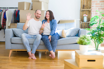 Fototapeta na wymiar Young couple sitting on the sofa arround cardboard boxes moving to a new house showing and pointing up with fingers number nine while smiling confident and happy.