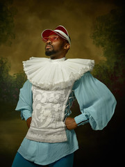 Young man as a medieval grandee or nobleman on dark studio background. Male model in a cap and sunglasses. Portrait in retro costume. Human emotions, comparison of eras and facial expressions concept.