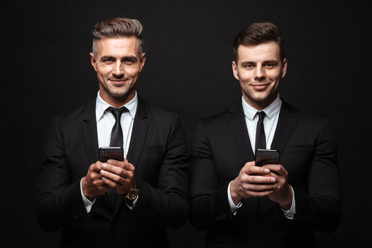 Adult business men posing isolated over black wall background using mobile phones.