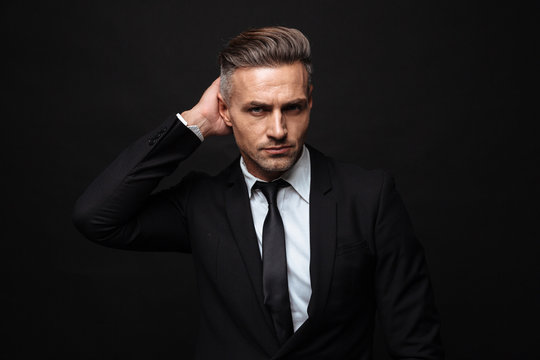 Handsome mature business man posing isolated over black wall background.