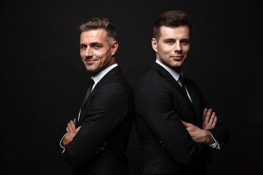 Handsome two adult business men posing isolated over black wall background.