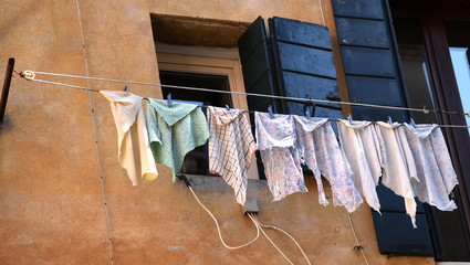 Kleidungsstücke auf einer Wäscheleide vor gelber Hausfassade mit blauem Fensterladen