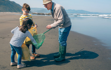 Grandfather and grandchildren taking garbage out of the sea with a fishing net