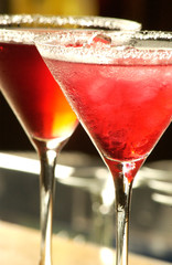 close up of two cocktail glasses with red frosted alcohol on bar 