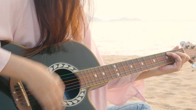 4K. close up of long hair woman playing acoustic guitar at the beach with gentle wind during sunset time, feeling relax
