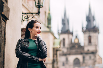 Fototapeta premium Street portrait of adorable brunette woman with long hair posing at Old Town Square in Prague. smiling pretty brunette girl, lifestyle. observatory of astronomical clock tower in Prague, Czech