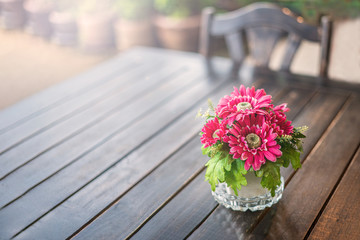 red and Burgundy beautiful flowers are on the wooden table on the right. there's a chair in the background. close-up, green blurred background. a summer café or a terrace.