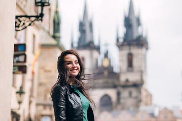 Fototapeta premium Street portrait of adorable brunette woman with long hair posing at Old Town Square in Prague. smiling pretty brunette girl, lifestyle. observatory of astronomical clock tower in Prague, Czech