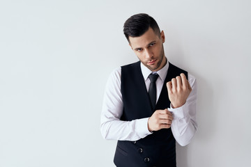 Handsome young man adjusting his sleeves and fixing his cufflinks against white background