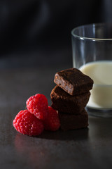 Stack of raspberries and chocolate brownies with a glass of milk. Vertical