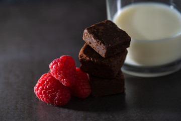 Stack of raspberries and chocolate brownies with a glass of milk.