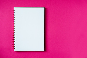 School notebook on a pink background, spiral notepad on a table. Top view copy space, mockup. Office notepad flat lay.