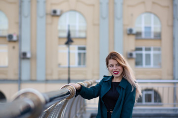 Fototapeta premium Closeup portrait of romantic blonde girl wearing green coat holding onto the rail. Space for text