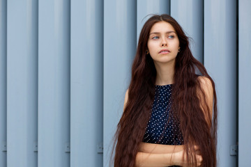 Alluring long haired young lady posing near the metal shutters at the street. Empty space