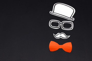 Paper cut hat, glasses, mustache and red bow on black background. Male face creative concept