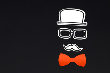 Paper cut hat, glasses, mustache and red bow on black background. Male face creative concept.