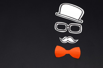 Paper cut hat, glasses, mustache and red bow on black background. Male face creative concept.