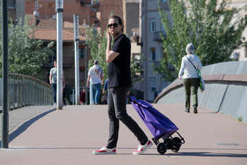 Hombre joven turista yendo a comprar con un carro de la compra y buscando piso o una casa para alquilar.