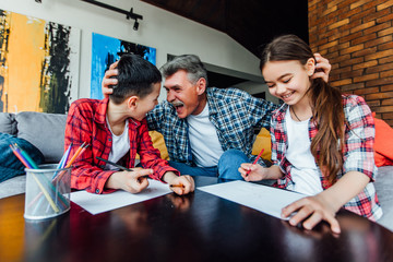 Family concept. Two grandchildren paint with grandfather on living room. Funny emotions.