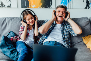 Happy elderly man with a little girl is using a headphones while lying at home...