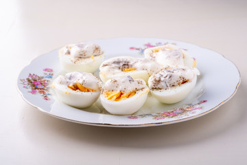 Sliced boiled eggs with mayonnaise and pepper in white plate isolated angle view