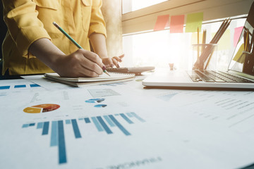 A woman using laptop computer to analysis data report during writing make note some data on notepad, Business financail concept