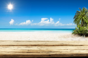 Fototapeta premium Wooden table background of free space and summer landscape of beach with palms and ocean. 