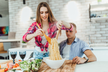 Portrait of cheerful positive partners preparing supper together, eat  macaroni on stove.
