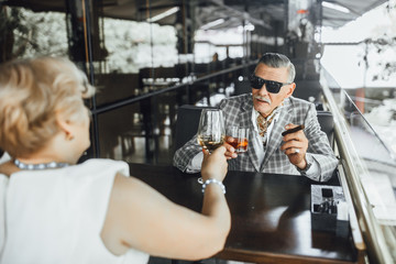Successful  senior man sit in the summer terrace with his  blonde woman ,testing expansive romm