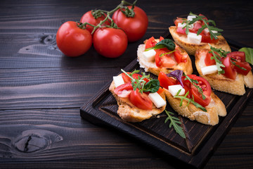 Bruschetta with tomatoes, mozzarella cheese and herbs on a cutting board in a dark background
