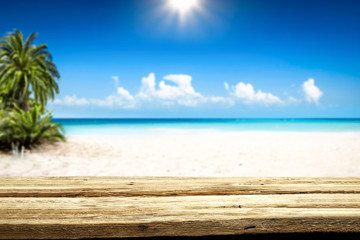 Fototapeta premium Wooden table background of free space and summer landscape of beach with palms and ocean. 