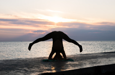 unrecognizable woman with beautiful body doing yoga headstand at sunrise on the sea, silhouette of yoga poses