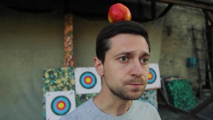 Portrait of fearful scared handsome man putting red apple on his head, being a target, prays and closes his eyes. Danger, stressful situation, extreme activities. Having fun, trust concept - Powered by Adobe
