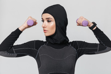 Young woman fitness muslim make exercises with dumbbells isolated over white wall background.