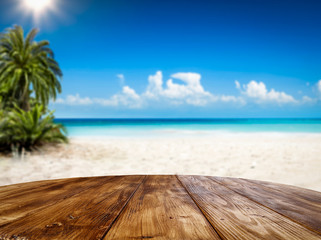 Fototapeta premium Wooden table background of free space and summer landscape of beach with palms and ocean. 