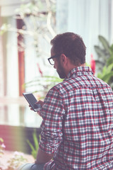 Modern bearded man using cellphone and drinking coffee with laptop.