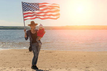Independence Day. Patriotic holiday. A woman in a cowboy hat with a baby in her arms and with an American flag.