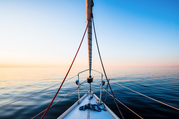 The calm water. White yacht sailing at sunset. A view from the deck to the bow, mast and the sails. Baltic Sea, Latvia