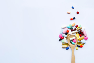 Colorful tablets, capsules and pills with wooden spoon on white
