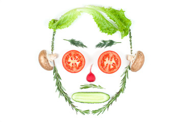 Funny face from different vegetables tomatoes, cucumber, radish, dill and rosemary isolated on white background. Healthy eating and vegan food concept. Kitchen