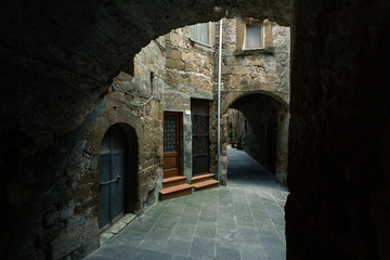 Fototapeta na wymiar Dark alley leads to light with an arch in old medieval Italian town. Narrow street
